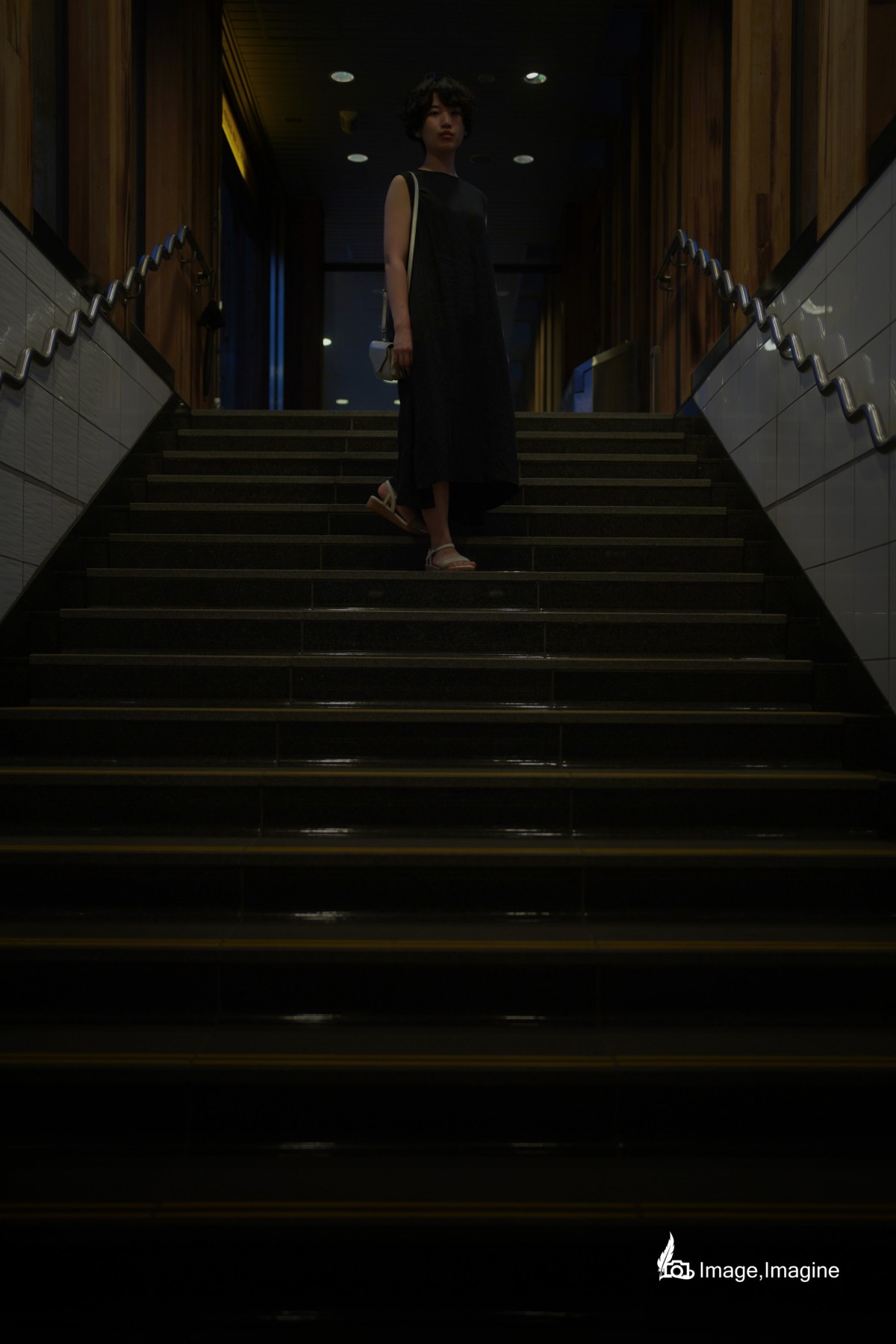 夜の街にて、地下へ続く階段で女性を撮影した写真。女性は全身黒いワンピースを着て、こちら見つめながら階段の中央で立っている。