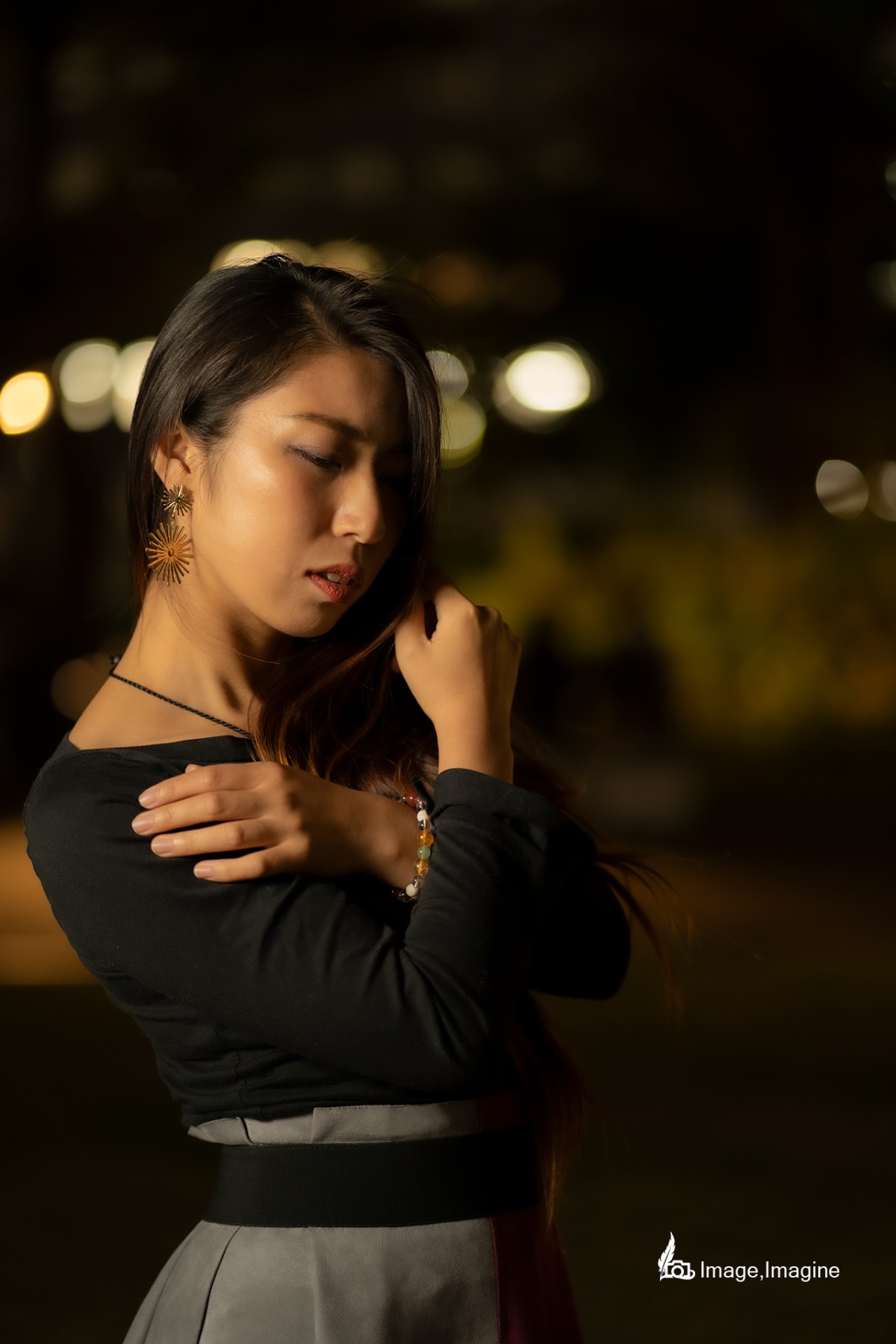 夜の街で女性を撮影した写真。女性は何かを包むように胸の上で両手をクロスさせ、どこか切なげな表情でややうつむいている。