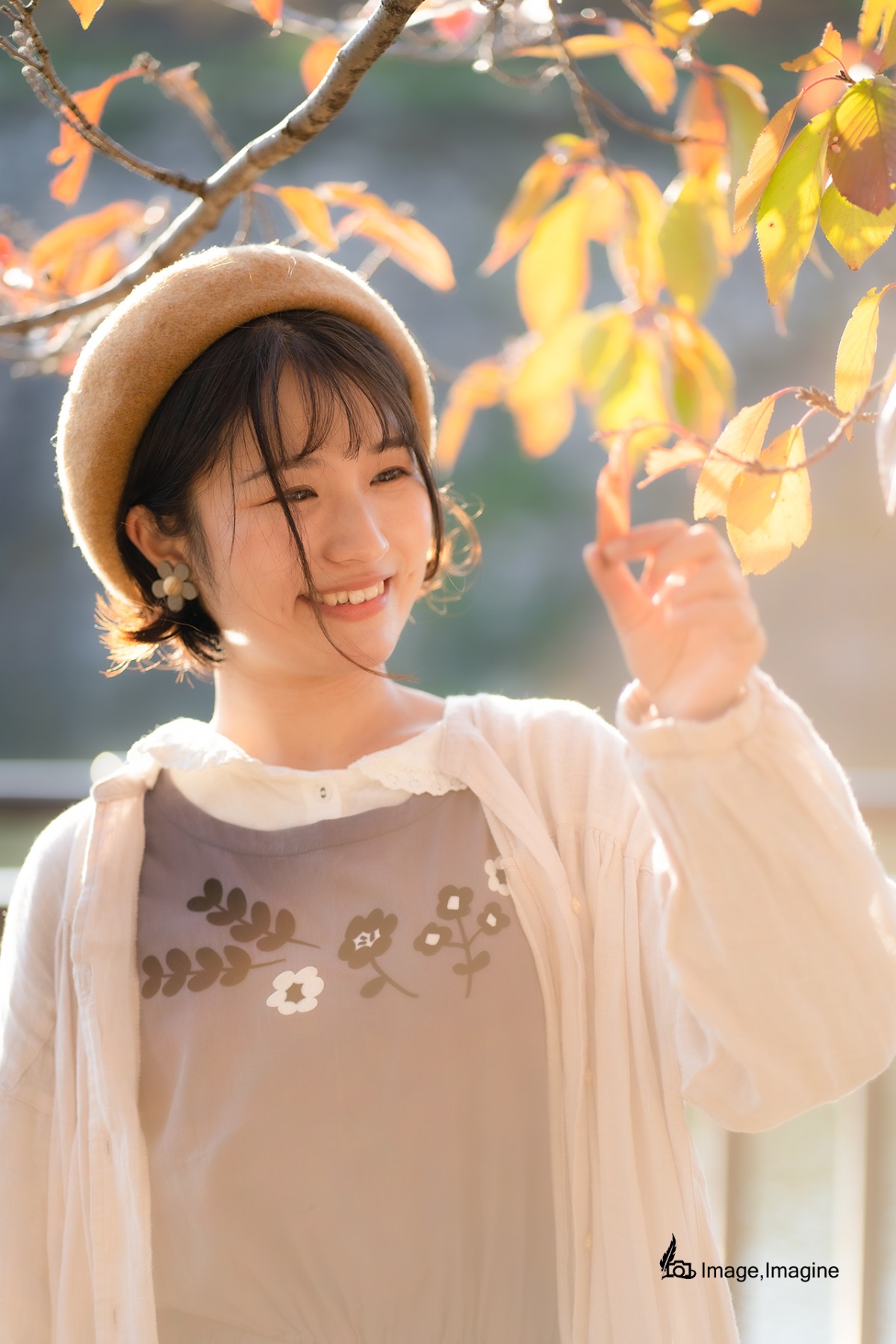 秋の大阪城で女性を撮影した写真。女性はオレンジ色に染まった木の葉を左手でつまみながら微笑んでいる。