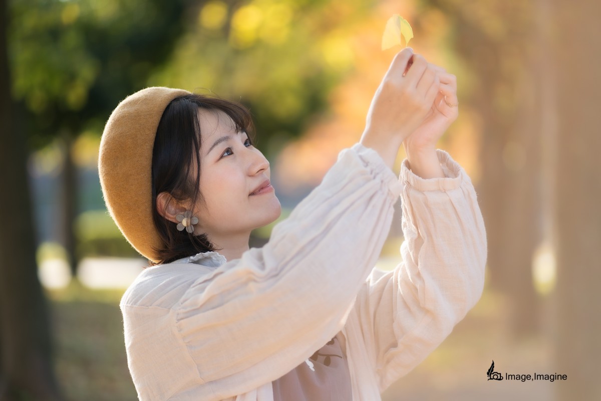 秋の大阪城で女性を撮影した写真。女性は黄色のイチョウの葉を空にかざすように両手で持ちあげている。